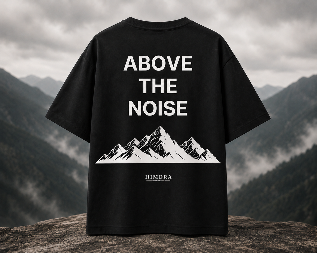 Black t-shirt with 'Above the Noise' and mountain design on a mountainous background