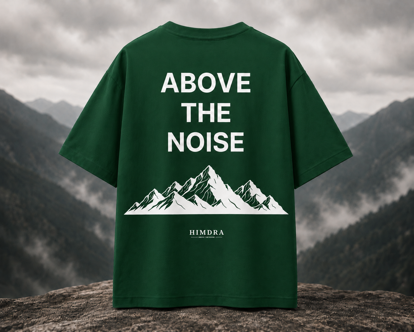 Green t-shirt with 'Above the Noise' and mountain design on a mountainous background