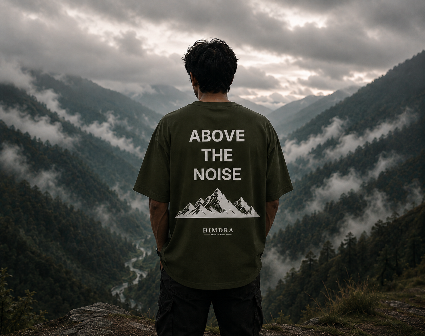 Person wearing a t-shirt with 'Above the Noise' design in a mountainous landscape